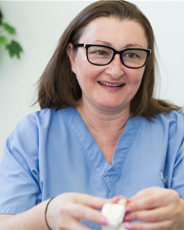 Dr. Anna Lekht in blue scrubs, smiling as she explains a tooth model to a patient
